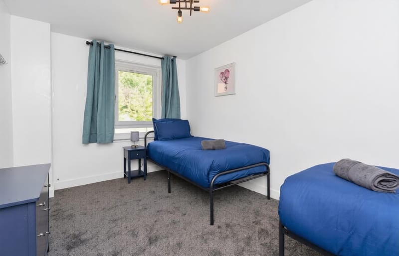 Bedroom with a single bed in blue linen and a teal curtain at the window.