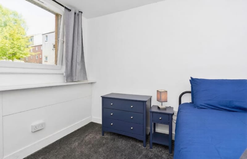 Bedroom with a single bed under the window, a navy chest of drawers, and a bedside lamp.