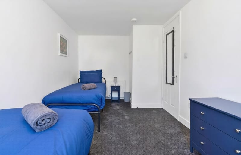Bedroom with a single bed in blue linen, a bedside table, and a chest of drawers by the door.