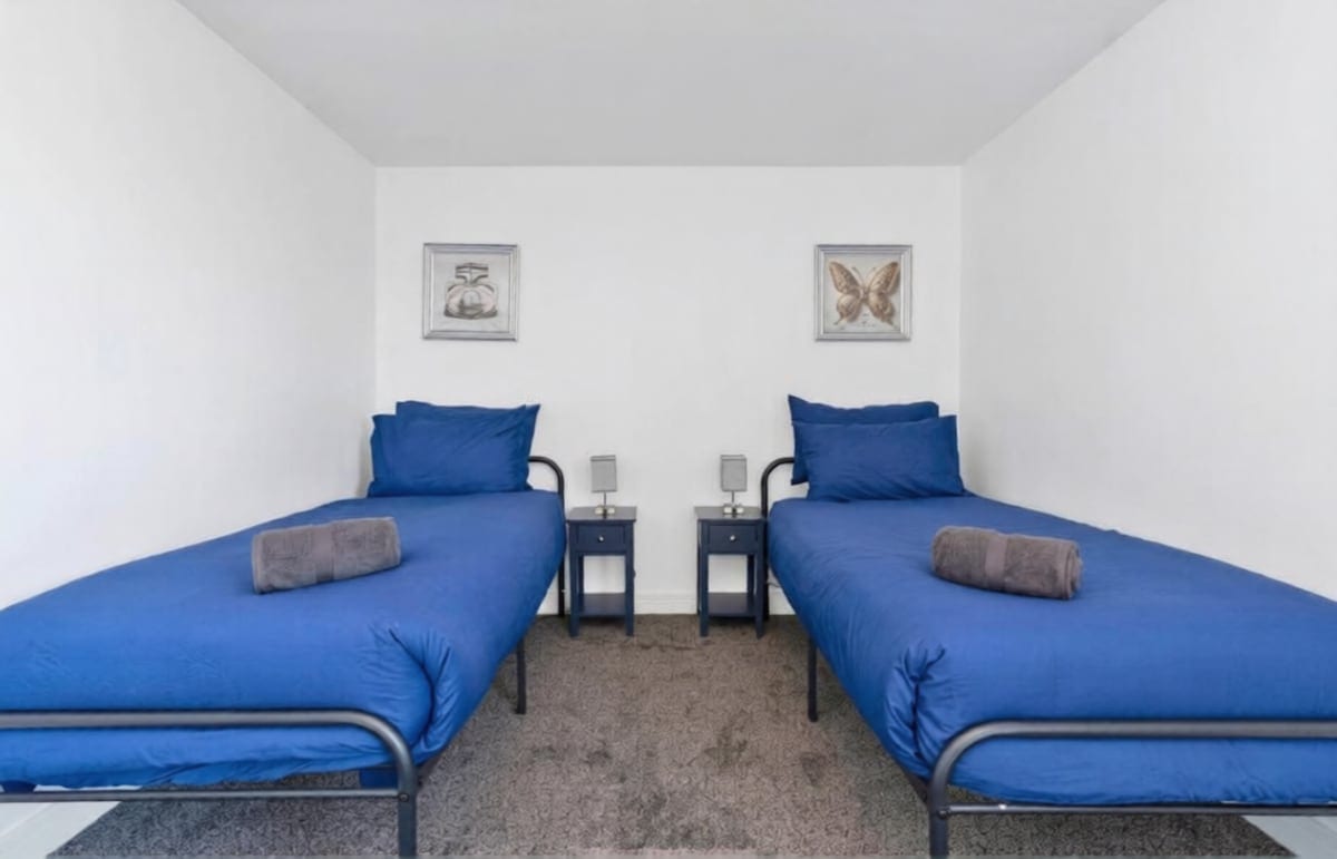 Twin bedroom with two single beds in blue linen, folded towels, and framed prints above the beds.