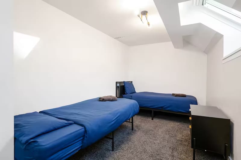 Twin bedroom with two single beds in blue linen, folded grey towels, and a skylight in the sloped ceiling.