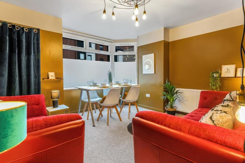 Dining table laid for four beside a red sofa and armchair, with a plant by the radiator.