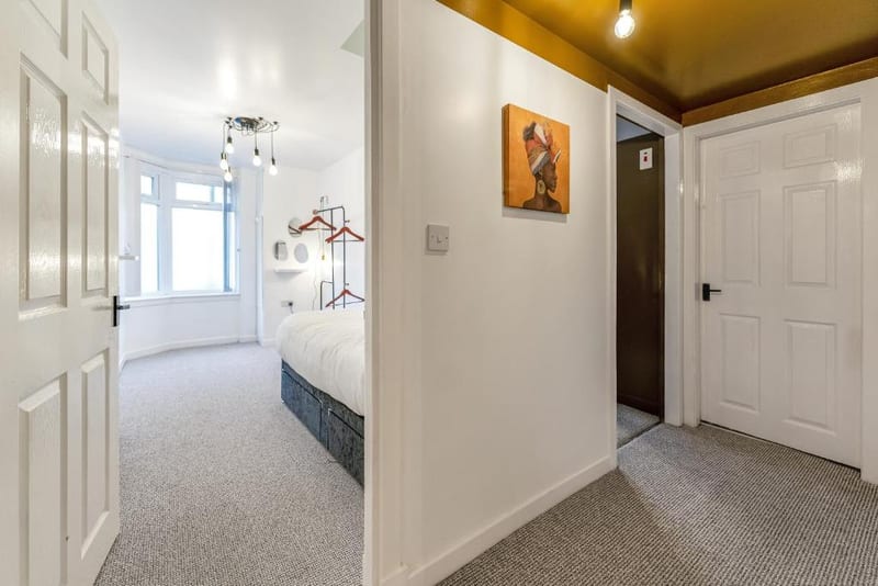 Hallway with white doors and a coat rack, looking through to a bedroom.