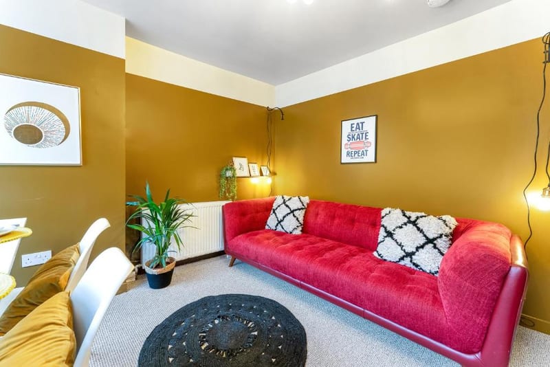 Red sofa against an ochre wall, with a round woven rug and a plant in the corner.