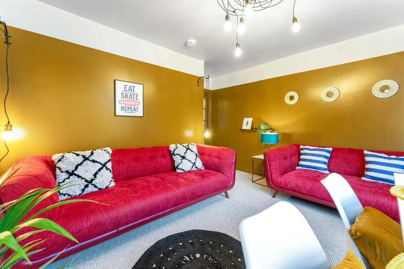 Sitting room with two red sofas, patterned cushions, and a framed print on the ochre feature wall.