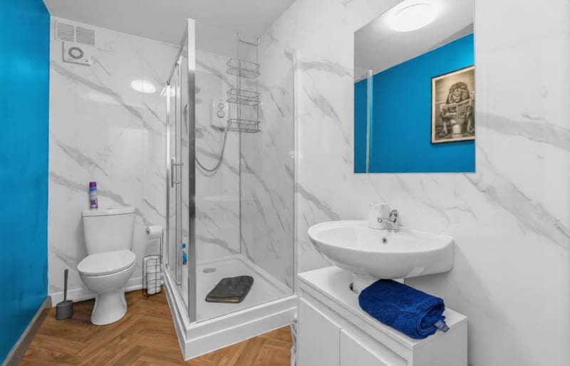 Shower room with a glass enclosure, a marble-effect wall, a wall-hung basin, and a blue painted alcove.