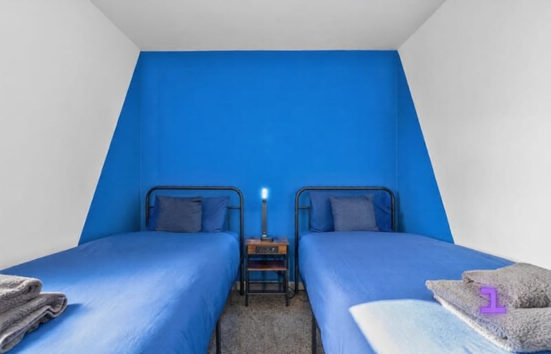 Twin bedroom with two single beds in blue linen against a blue feature wall, with folded towels at the foot.