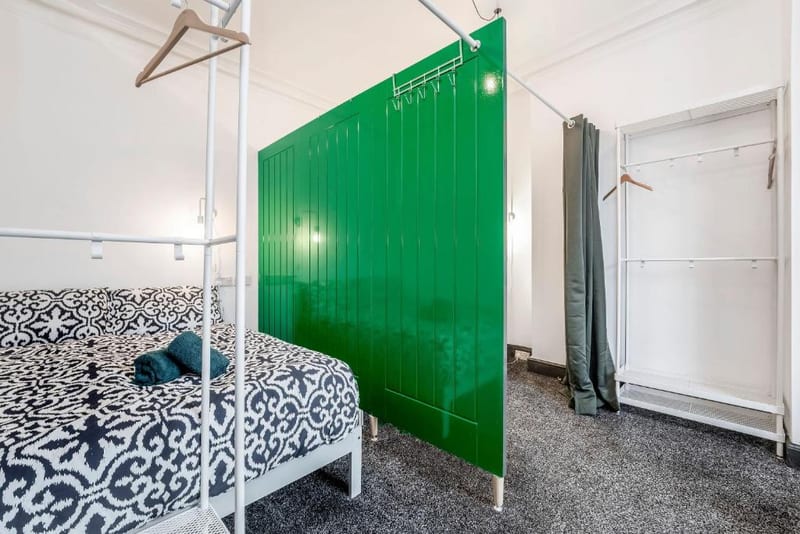 Double bed with a black and white patterned cover beside a green panelled divider, with an open clothes rail and hangers.