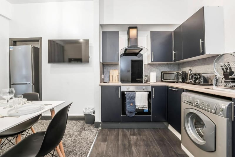 Kitchen with dark grey units, an oven under an extractor hood, a microwave, a toaster, a washing machine and a tall fridge freezer.