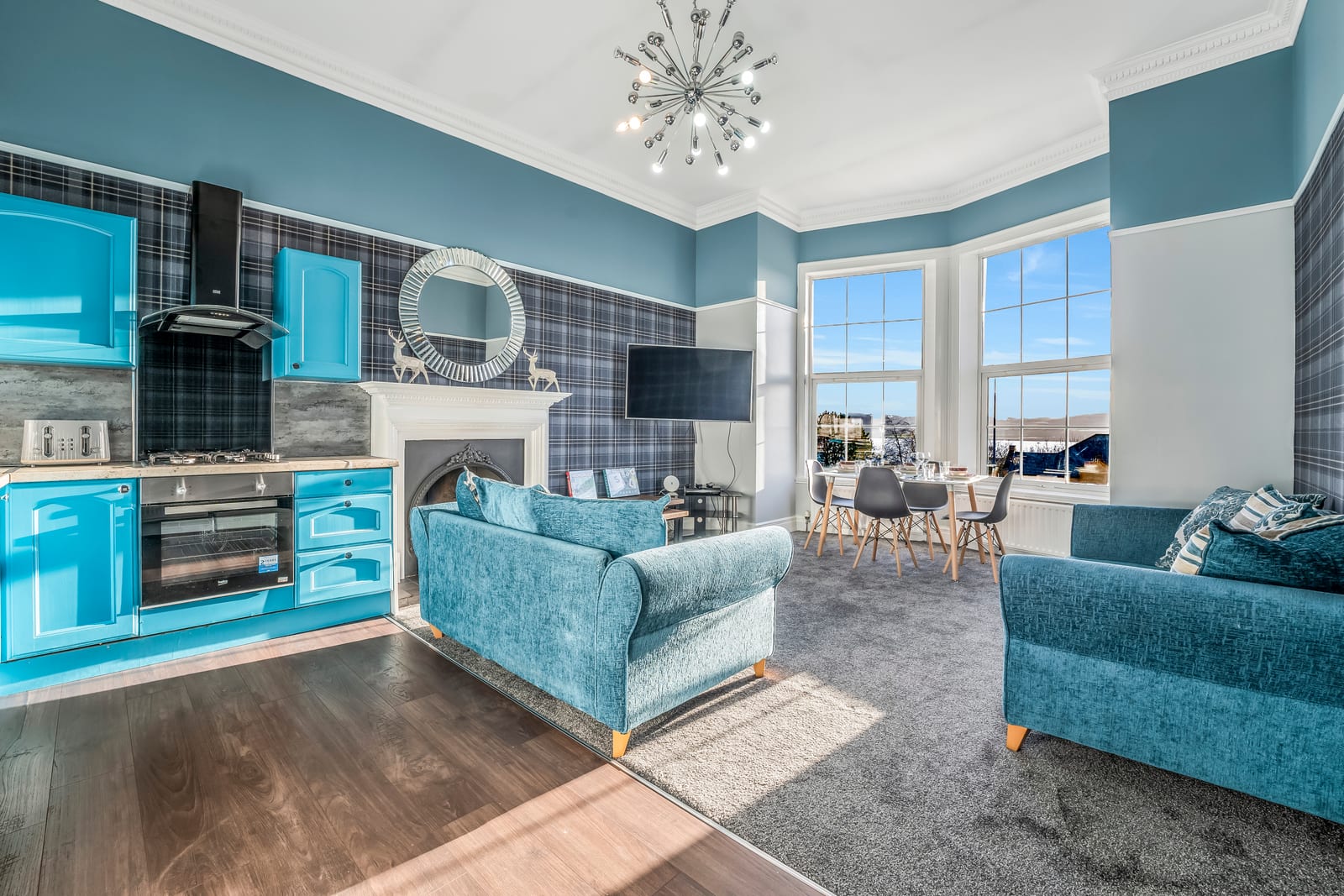 Living room with a teal fireplace surround, a round mirror above it, two teal sofas and a bay window onto the street.