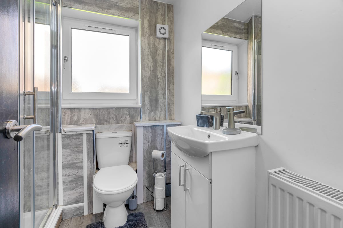Shower room with a glass enclosure, a WC and a basin set into a vanity unit, lit by two frosted windows.