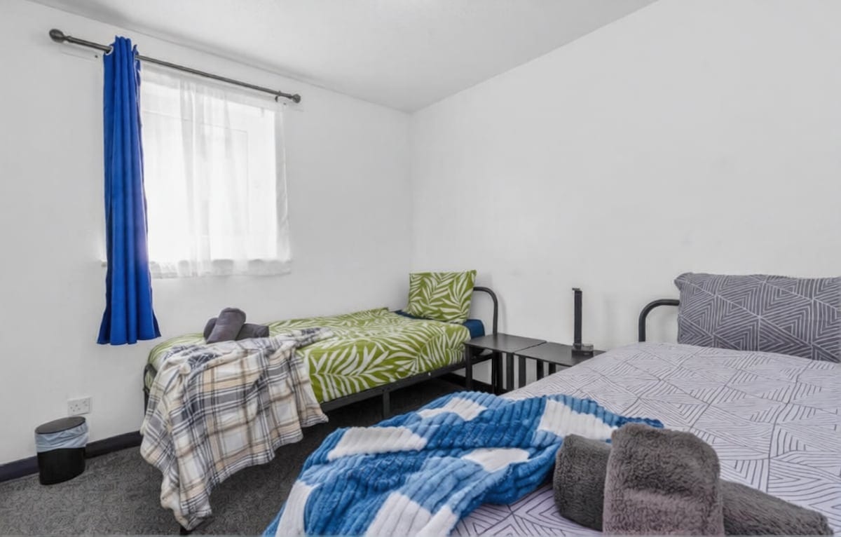 Twin bedroom with two single beds, blue curtains, and folded grey towels.
