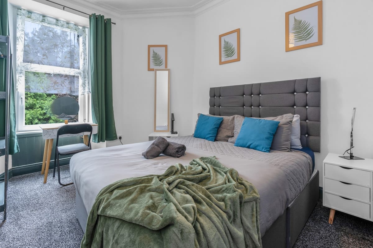 Double bedroom with a grey buttoned headboard, a green throw, and a desk in the bay window.