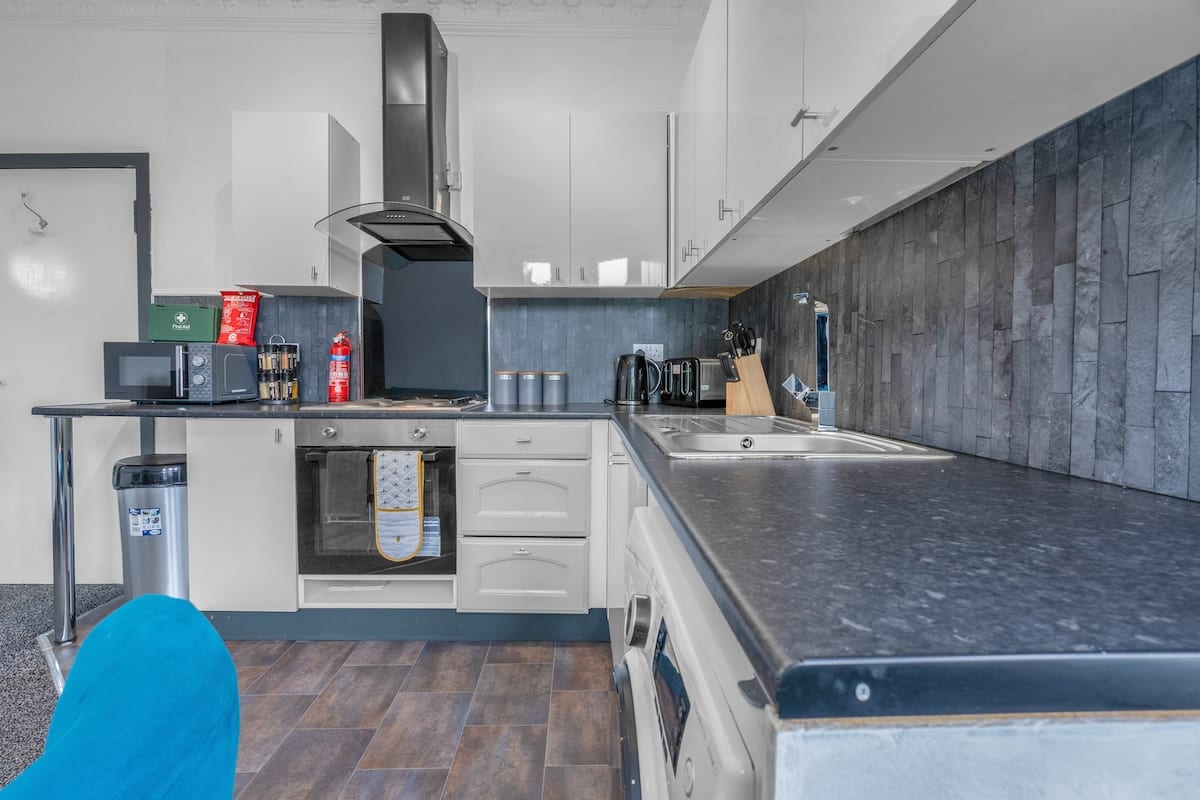 Galley kitchen with white units, a slate-effect splashback, and an extractor over the hob.