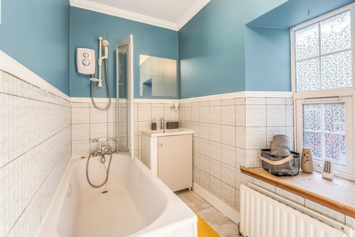 Bathroom with a bath and shower over it, white tiling, and a pale blue wall.