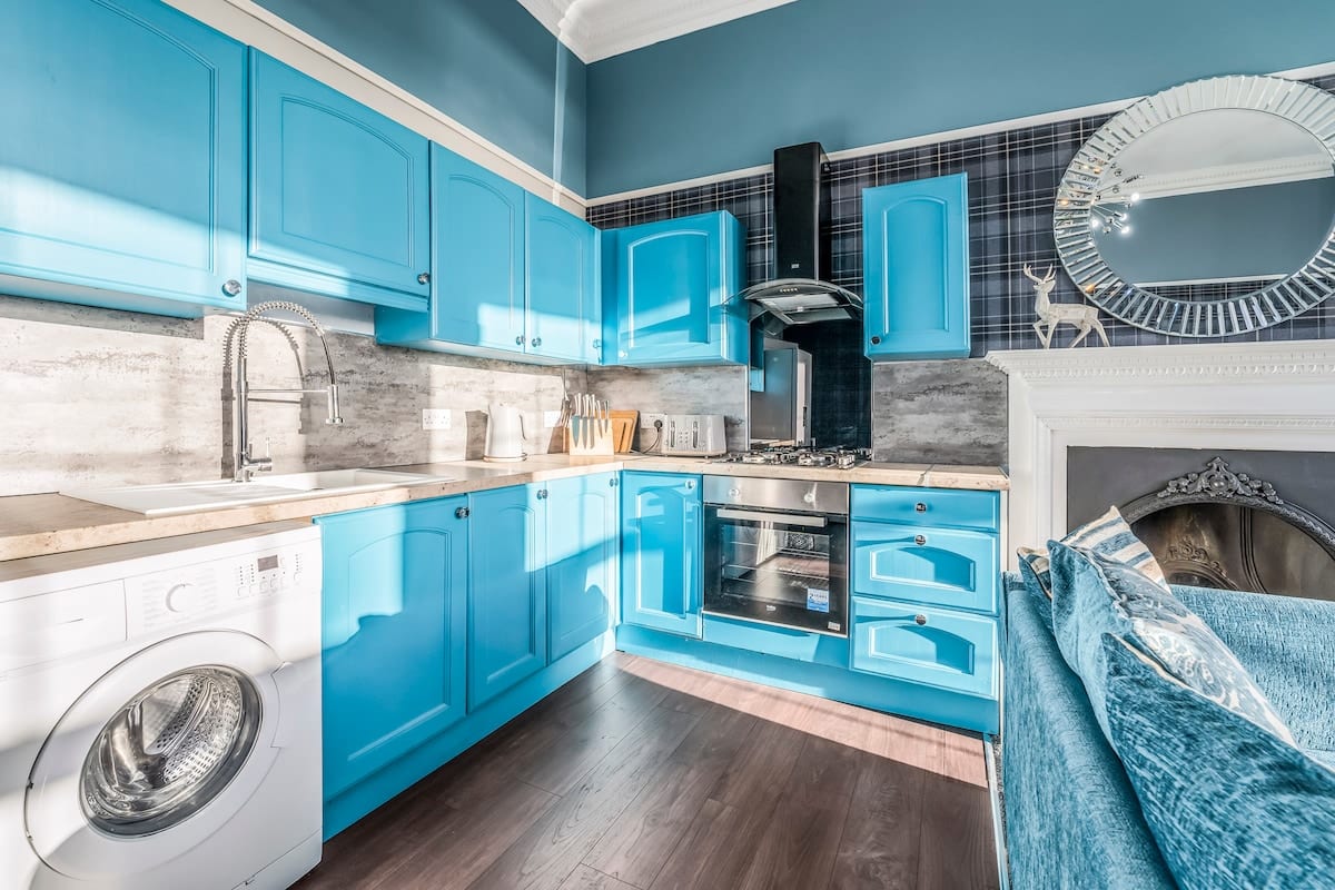 Teal kitchen with a washing machine, an oven, and a mirror above the fireplace.