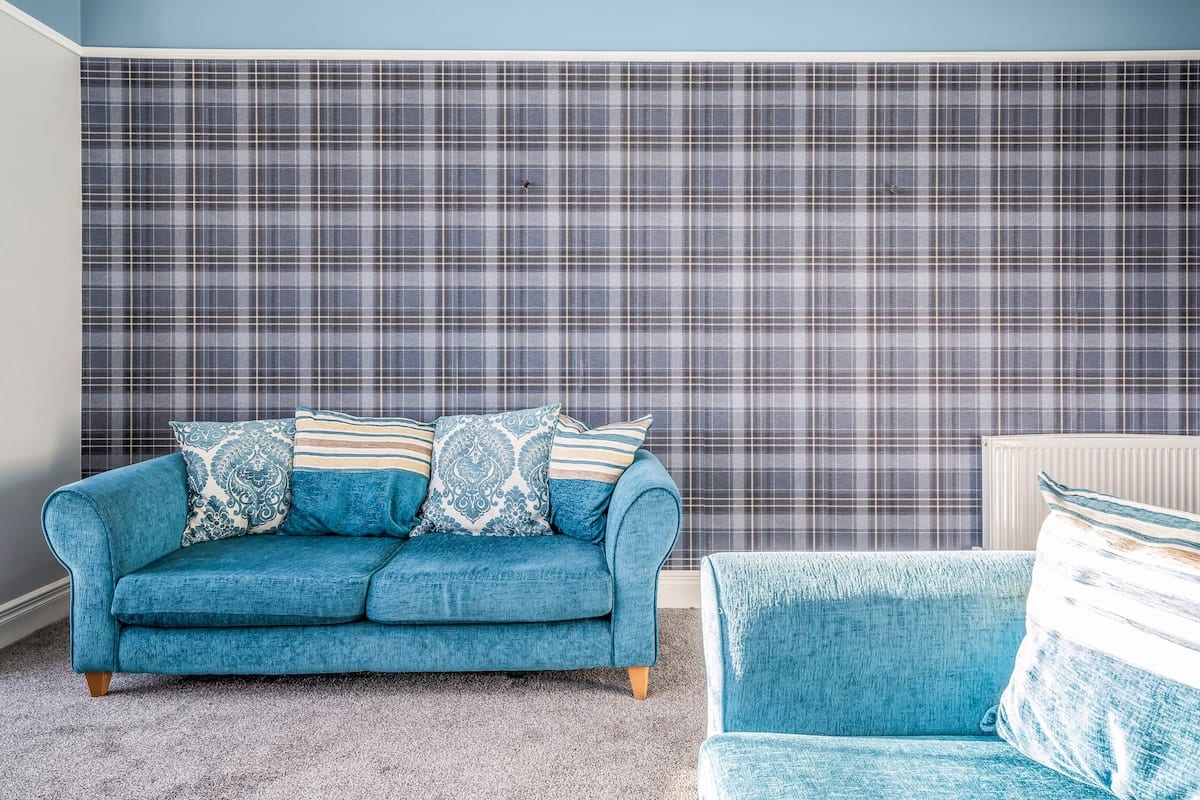 Teal sofa against a tartan papered wall, with a second sofa alongside.