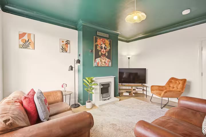 Living room with a white fireplace, a television on a stand, brown leather sofas and a tan velvet armchair.