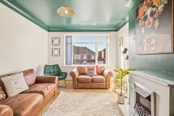 Living room from the doorway, with the bay window, a green velvet chair and a two-seat leather sofa.